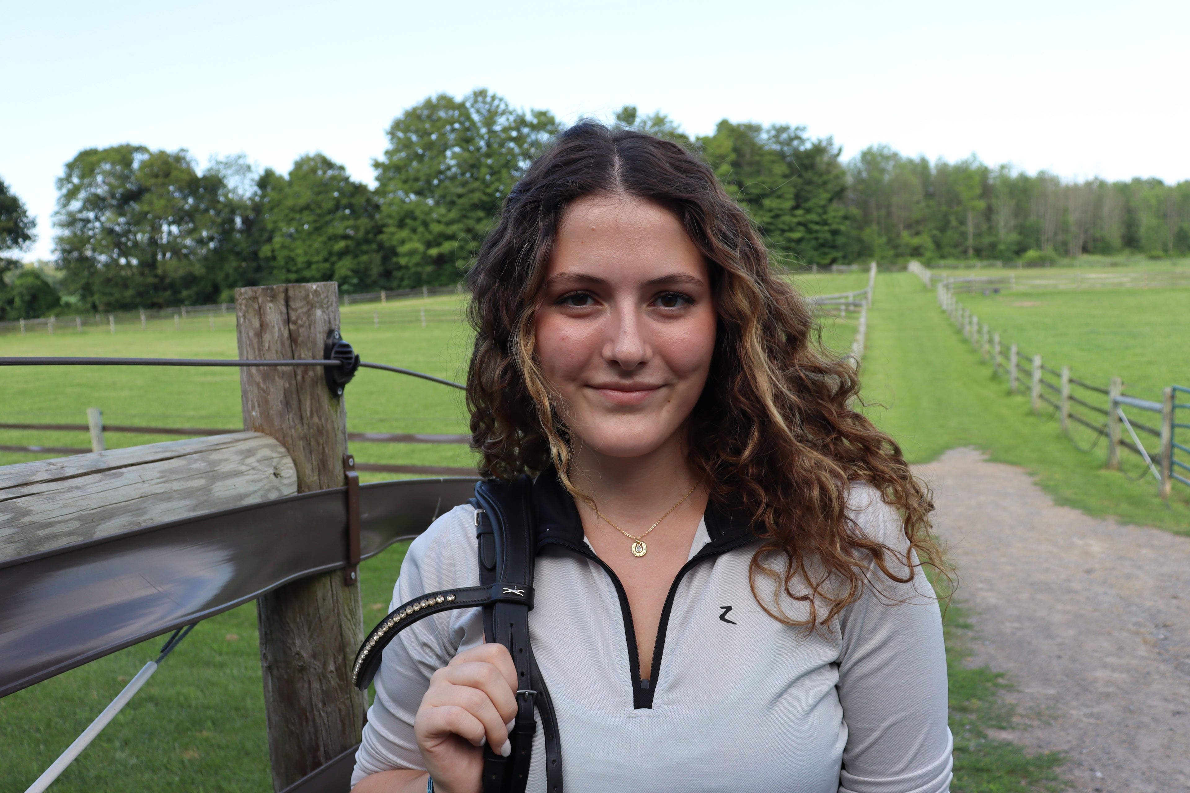 girl holds bridle on her shoulder wearing gold horse shoe necklace