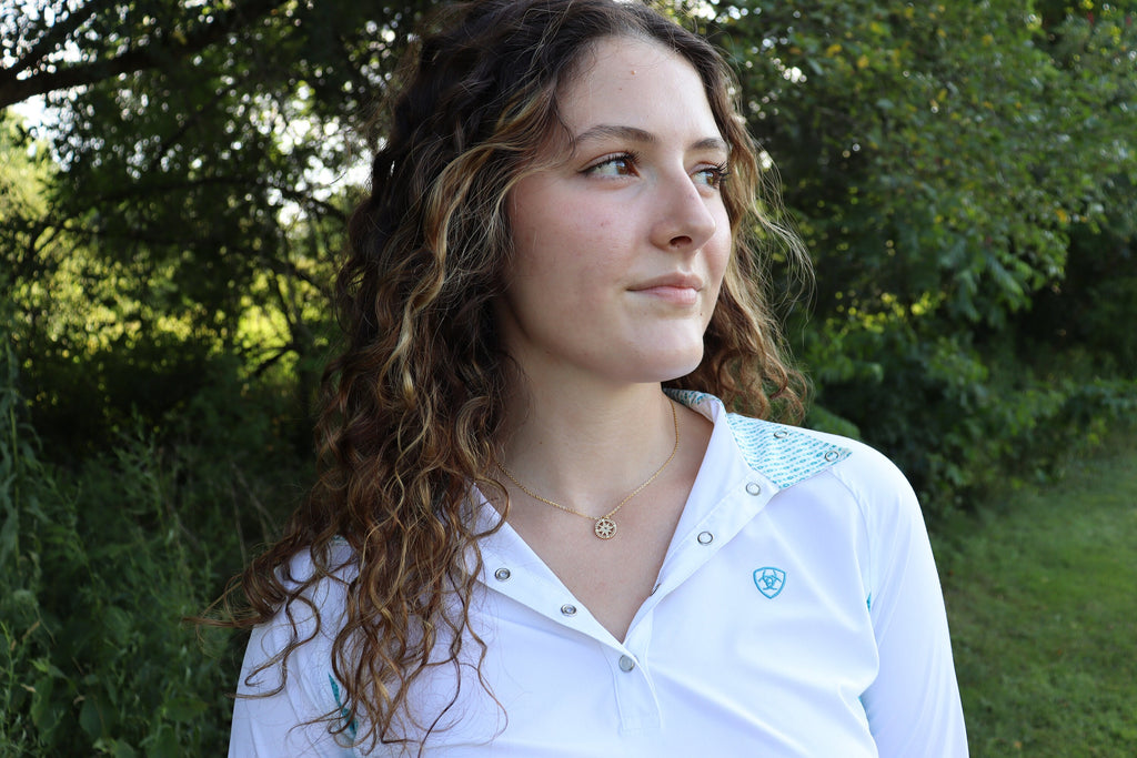 girl in white button up and compass necklace looks off to the side