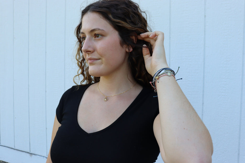 girl pushes hair behind ear showing off gold necklace